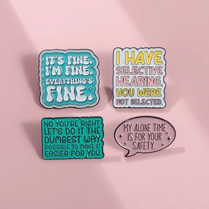 Détail de quatre épinglettes en émail coloré avec citations drôles sur fond rose