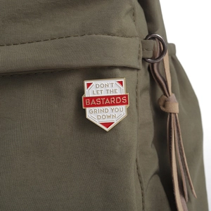 Macro view of shield-shaped enamel pin with motivational text on green fabric texture