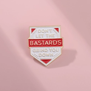 Close-up of shield enamel pin with Don't Let The Bastards Grind You Down text