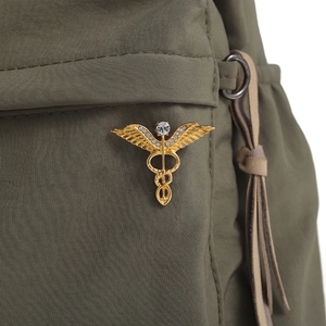 Close-up of golden Caduceus medical brooch with rhinestones on green fabric bag