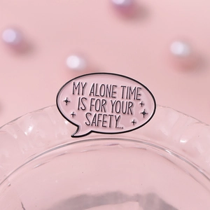 Broche en émail rose en forme de bulle avec texte d'humour posée sur un verre