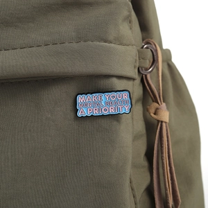 Detail of MAKE YOUR MENTAL HEALTH A PRIORITY enamel pin on a dark canvas bag