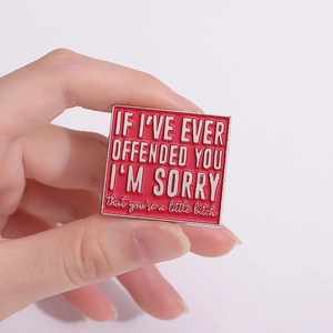 Square red enamel pin with silver metal frame and sarcastic English quote on a bag