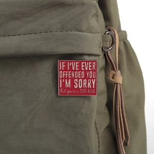 Square red enamel pin with silver text on green canvas bag, artistic funny quote badge