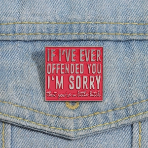 Close-up of a red enamel pin with silver text on a blue denim jacket pocket