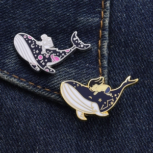 Close-up of enamel whale pins featuring astronaut and starry night motifs on denim