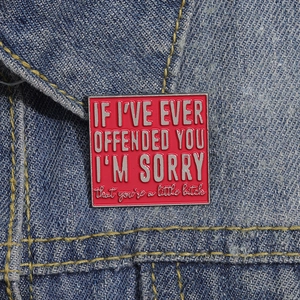 Macro shot of red enamel square brooch with sarcastic text on a blue denim jacket