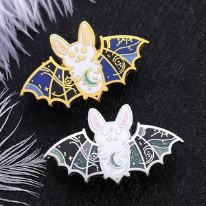 Close-up of gothic punk bat enamel pins with celestial patterns and moon details on black background