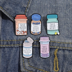 Set of 5 colorful enamel medicine bottle pins with Take Your Meds text on denim