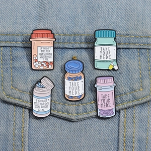 Detail of colorful pill bottle enamel pins with Take Your Meds slogans on denim jacket