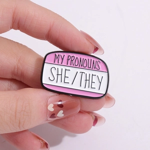 Cartoon enamel pin featuring pink and white My Pronouns She They design for clothes