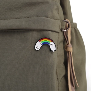 Detail view of rainbow ghost enamel pin attached to an olive green canvas bag