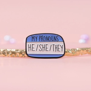 Pronouns enamel pin with HE/SHE/THEY text on a blue and white nameplate badge