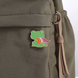 Detail of frog enamel pin with pride flag cape on a green backpack strap