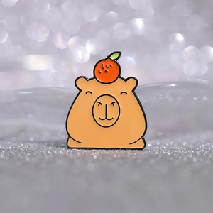 Macro d'une broche en émail de capybara avec une orange sur un fond argenté scintillant