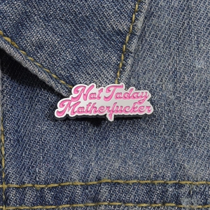 Spilla in smalto rosa con frase motivazionale appuntata su tessuto denim blu