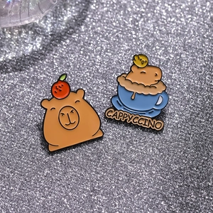 Détail macro de broches en émail capybara mignonnes avec texte Cappyccino sur fond pailleté