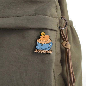 Détail du pin's émaillé capybara Cappyccino sur tissu olive montrant la texture de la laque