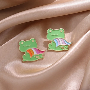 Cute green frog enamel pins with colorful pride flags on elegant champagne satin background