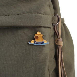 Enamel capybara bath pin with yellow ducks pinned on an olive green canvas bag