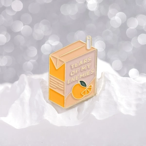 Pink orange juice box enamel pin with Tears of My Enemies text and golden straw detail