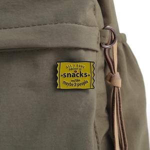 Makroaufnahme einer gelben Emaille-Anstecknadel im Snack-Design an einem Rucksack
