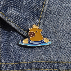 Close-up of cute enamel capybara and ducks pin pinned on blue denim fabric