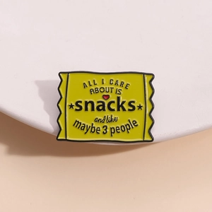 Lustige gelbe Emaille-Brosche in Snack-Tütenform mit Spruch auf weißem Podest