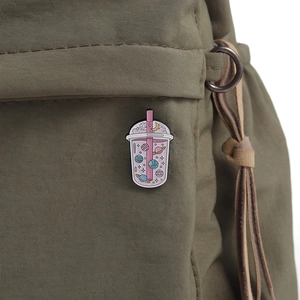 Detailed enamel pin of a space-themed bubble tea cup attached to a green canvas backpack