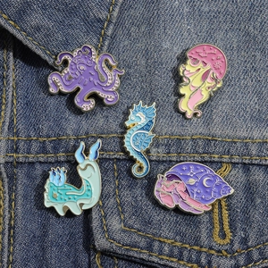 Detail von Meerestier-Emaille-Pins mit Sternen- und Mondmustern auf einer Denim-Jacke