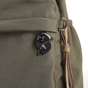 Detail of grim reaper enamel pin with scythe on olive green canvas bag background