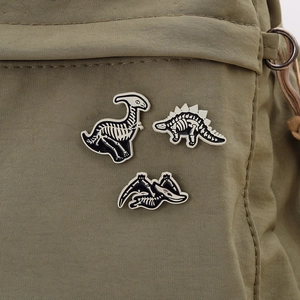 Three punk style dinosaur skeleton enamel pins pinned on a green canvas bag background