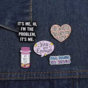 Five unique enamel pins with inspirational text and icons on blue denim background