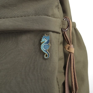 Detail einer blauen Seepferdchen-Brosche auf einer grünen Canvas-Tasche aus Stoff