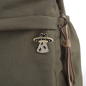 Macro detail of a black cat UFO enamel pin on a green textured bag with golden edges
