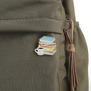 Detail of coffee cup and books enamel pin with Sorry I'm Booked text on green canvas bag