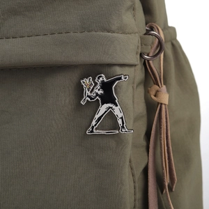 Detail shot of a Banksy Flower Thrower enamel pin pinned to a green canvas backpack