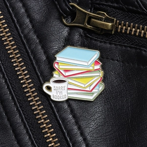 Detail of colorful book and coffee cup enamel pin on leather jacket with text Sorry I'm Booked