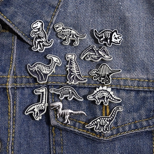 Detailed set of twelve punk style black and white dinosaur skeleton enamel pins on denim