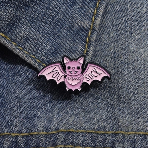 Detail der rosa Fledermaus-Emaille-Anstecknadel mit Text auf Denim-Stoff