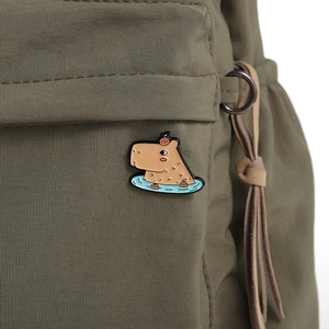 Detailed view of a cute capybara enamel pin with an orange on head on a green canvas bag