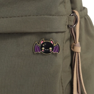 Detailed close-up of a cartoon bat enamel pin with purple wings on green canvas