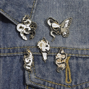 Detailed close-up of snake and butterfly enamel pins on a blue denim jacket pocket