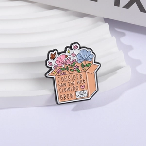 Enamel brooch with wild flowers in a box and Luke 12:27 quote on a white wavy stand