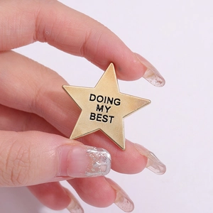 Star-shaped gold alloy badge pin with 'DOING MY BEST' slogan held by hand