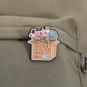 Enamel brooch with wildflowers and bible quote on orange box pinned to olive green bag