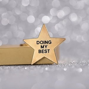 Detail of a gold star badge with Doing My Best engraving on a polished metal surface