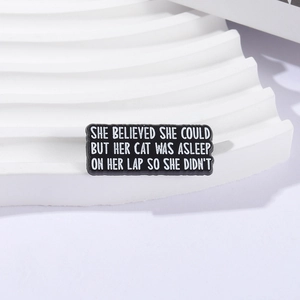 Funny black enamel cat brooch with white text slogan on a modern minimalist display