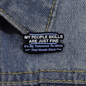 Macro shot of a black enamel pin with funny quote attached to a blue denim jacket