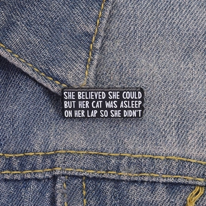 Funny black cat slogan enamel pin displayed on a blue denim jacket pocket